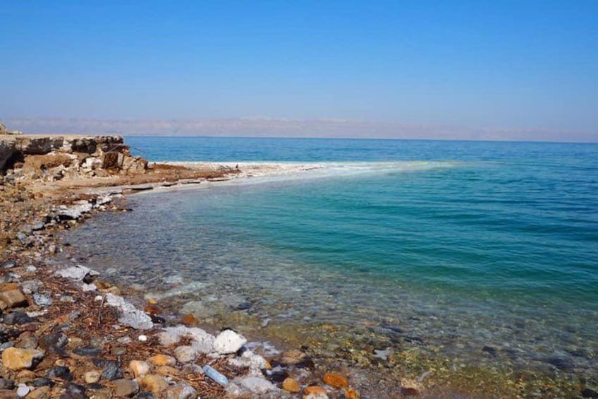 A rocky shoreline with clear blue water, a sandy beach, and distant mountains. 3