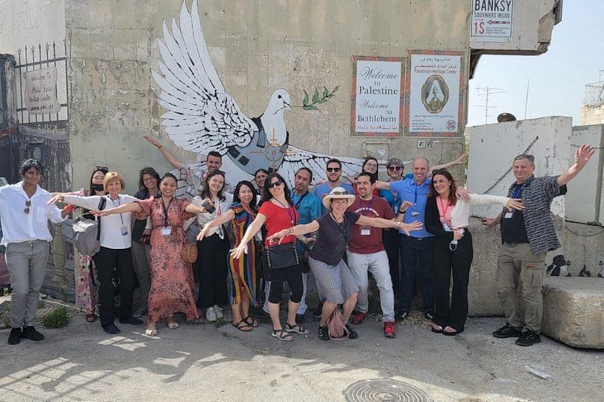 A group of people posing in front of a wall with a dove mural and signs. 3