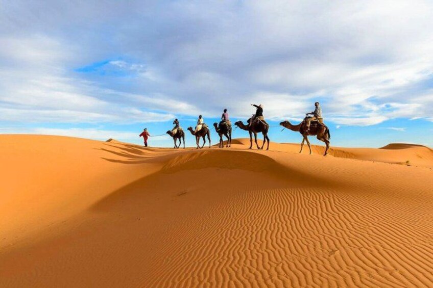 A group of people riding camels across a desert landscape with sand dunes. 1