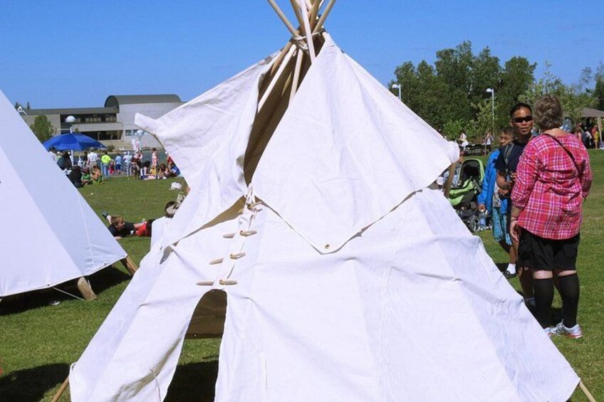 Een witte tipi met houten frame, opgesteld op het gras, met andere tenten op de achtergrond. 5