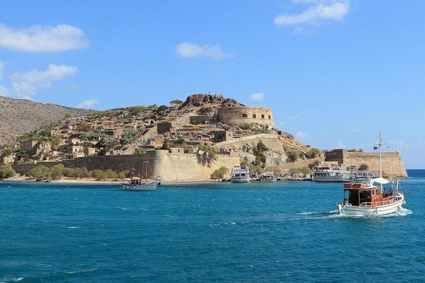 A coastal town with a historic fortification, boats in the water, and a clear blue sky. 1