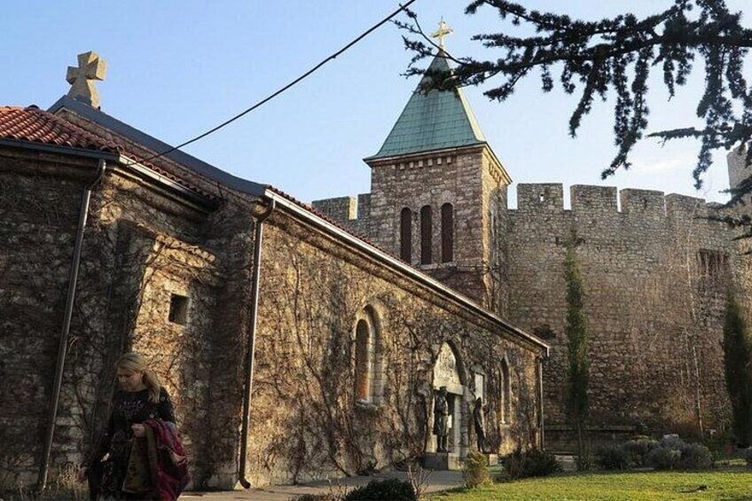 Un edificio de piedra con una torre de campanas, una persona caminando y un castillo al fondo. 4
