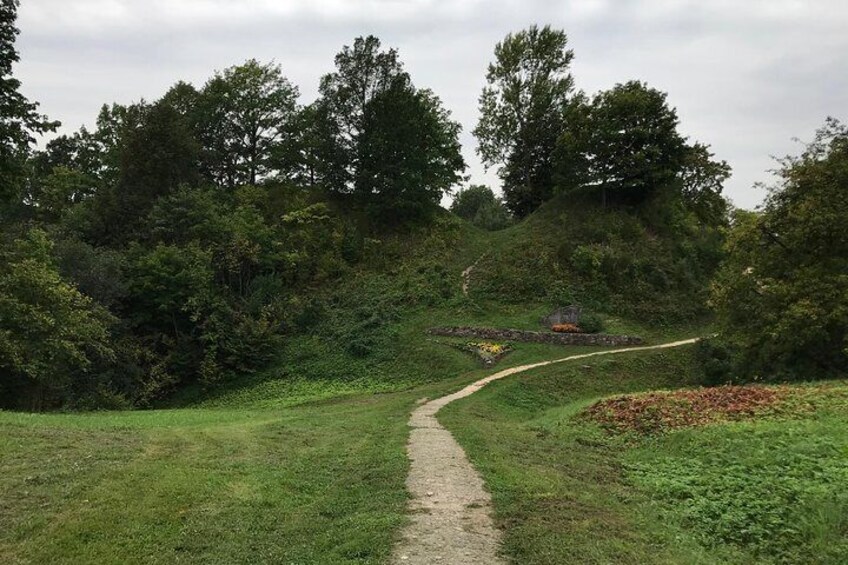 Een kronkelend pad door een grasrijk gebied, met bomen en een stenen gebouw in de verte. 2