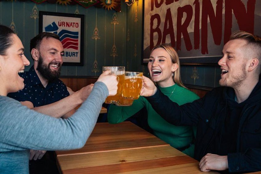 Un grupo de personas brindando con vasos de cerveza en un bar con un letrero que dice 'UR NATO BURT'. 5