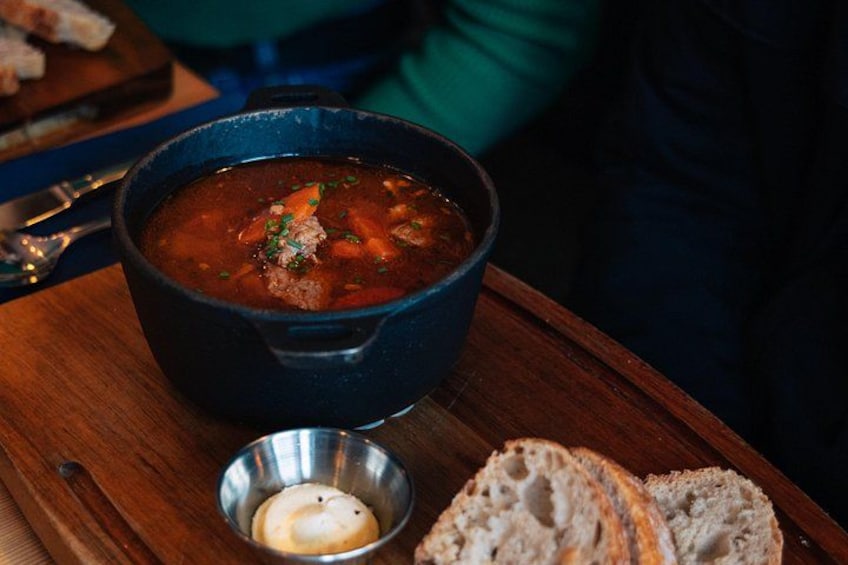 En skål suppe med en lille smørskål og skiver brød på et træbord. 2
