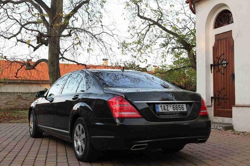 Ein schwarzes Auto auf einem Backsteinpflaster, im Hintergrund ein Baum und ein Gebäude. 2