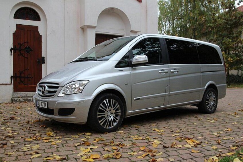 Ein silberfarbener Mercedes-Benz Minivan steht auf einer gepflasterten Auffahrt vor einem weißen Gebäude mit einer braunen Tür. 5