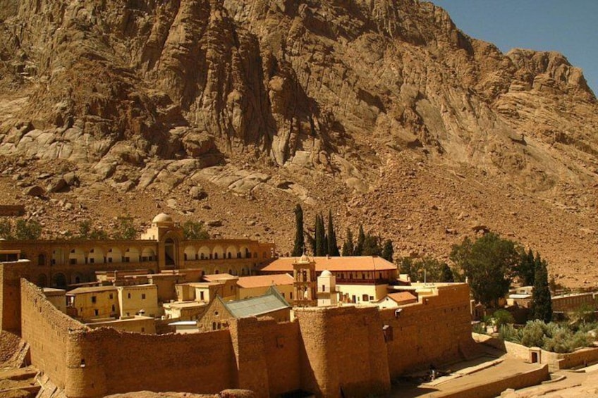 A fortified historical site with ancient architecture, a large mountain in the background, and a clear sky. 1