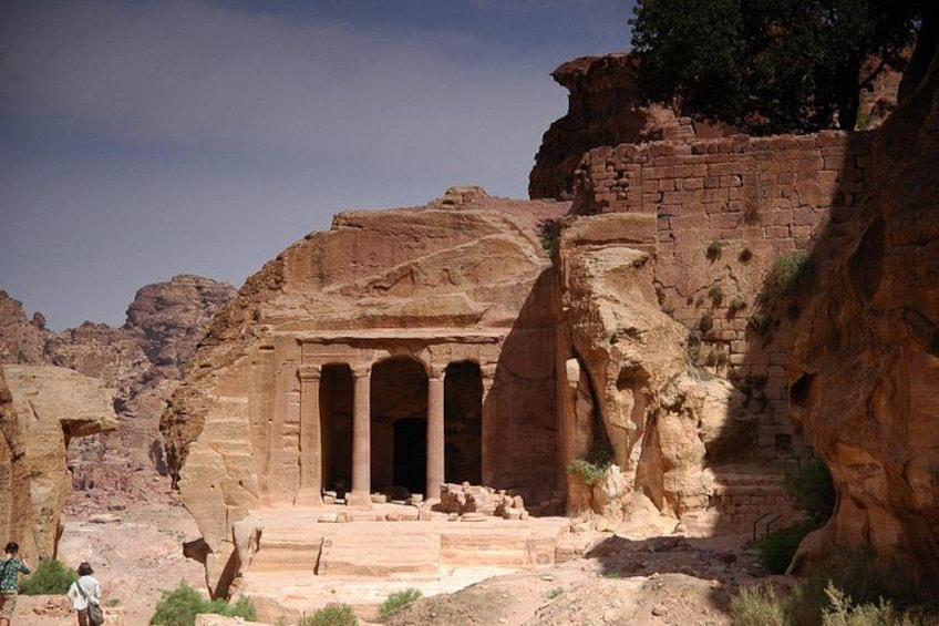 A historical site with a large rock-cut structure featuring columns and a staircase leading up to it. 3