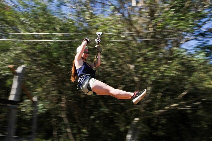 En person suser afsted i et zipline-anlæg gennem et skovområde. 1