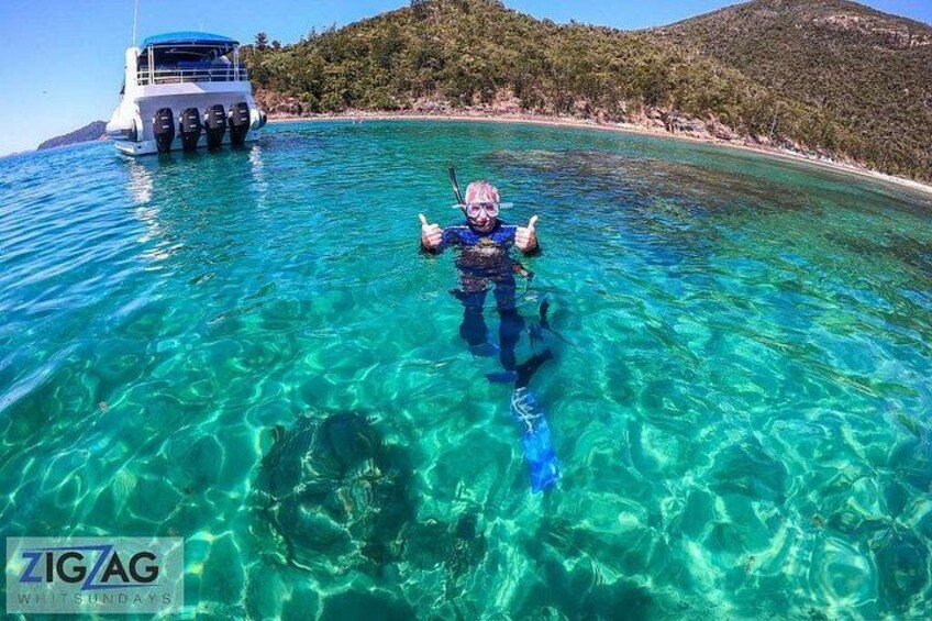 Una persona practica snorkel en aguas turquesas cristalinas, con un bote al fondo. 5