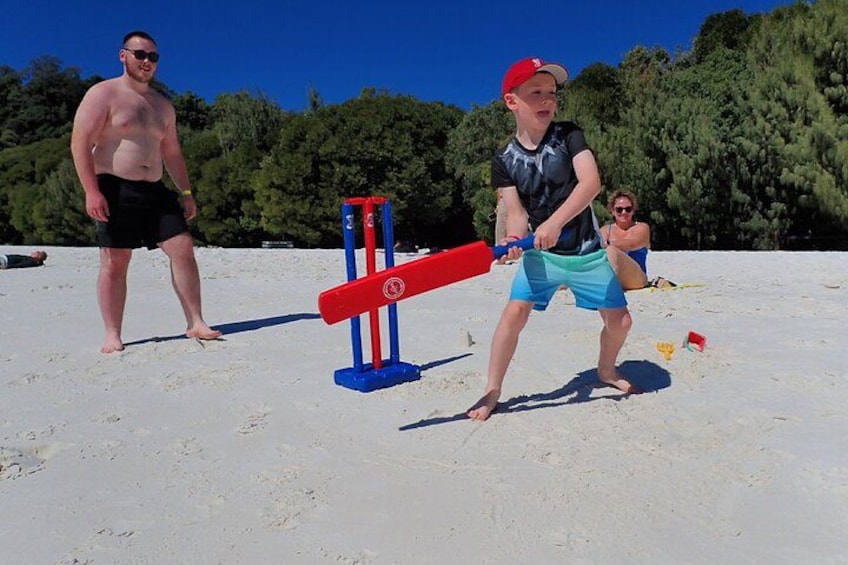 A person playing a game with a red and blue bat on a sandy beach with trees in the background. 4