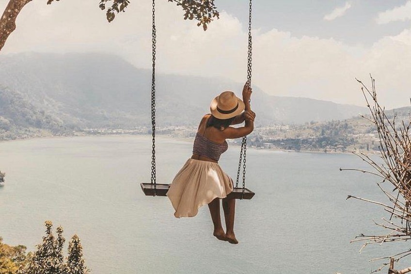A person on a swing over a body of water with mountains in the background. 2