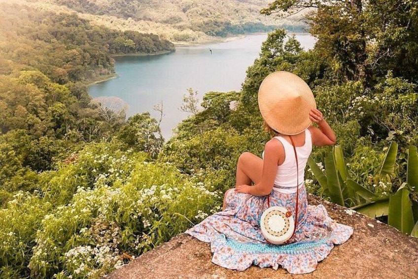 Une personne assise sur un rocher, avec vue sur un lac entouré de verdure. 2
