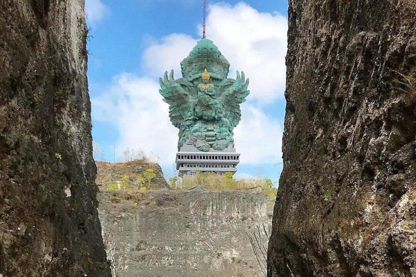 Una gran estatua de piedra con alas, un edificio y un paisaje rocoso. 2