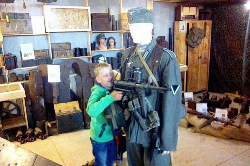 Una persona con camisa verde apuntando un rifle a un maniquí vestido con uniforme militar. 1