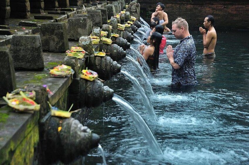 A water feature with multiple streams, people in the water, and offerings on the ledges. 2