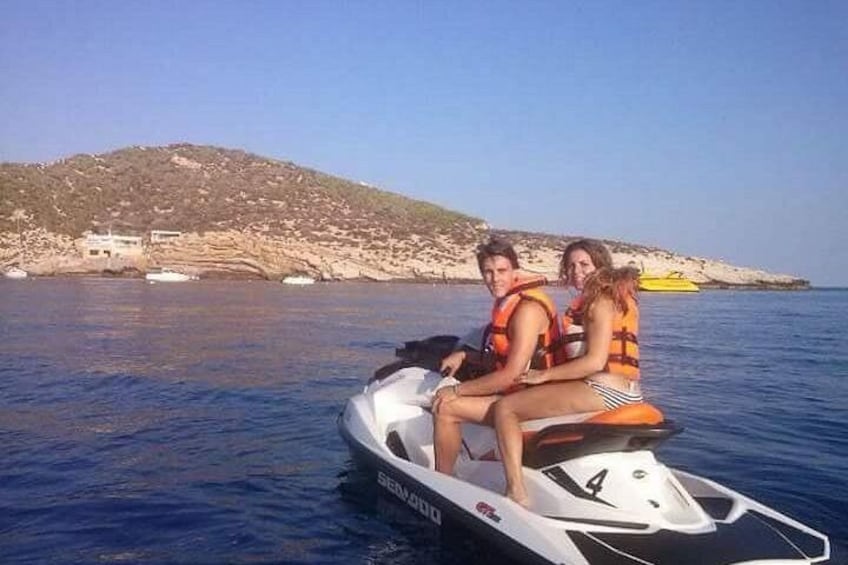 A jet ski on calm water with a rocky coastline and a hill in the background. 1
