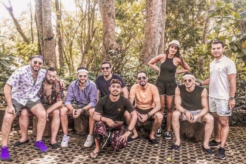 A group of people posing outdoors in a forested area with trees and a patterned ground surface. 2