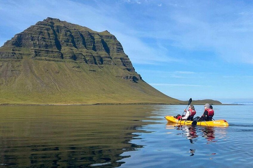 A kayaker and a companion on a calm body of water with a large, layered mountain in the background. 2
