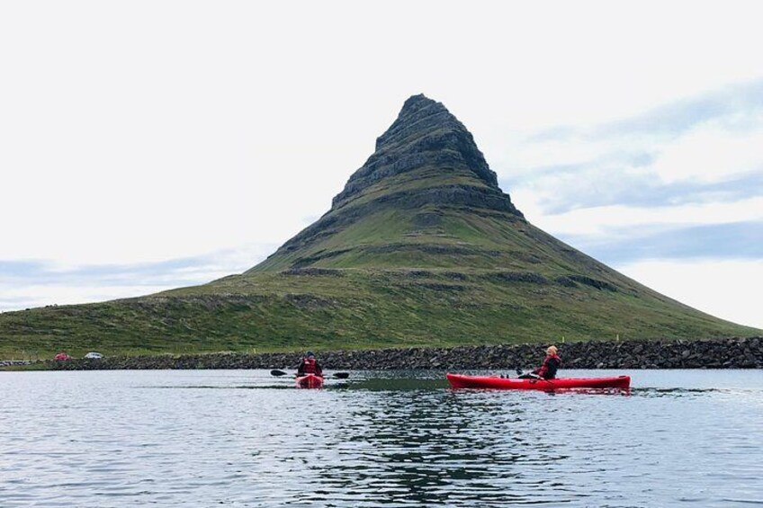 Two people kayaking on a calm body of water with a large hill in the background. 1