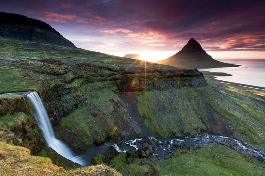 Une cascade, un paysage verdoyant et une montagne, avec le soleil couchant à l’horizon. 2