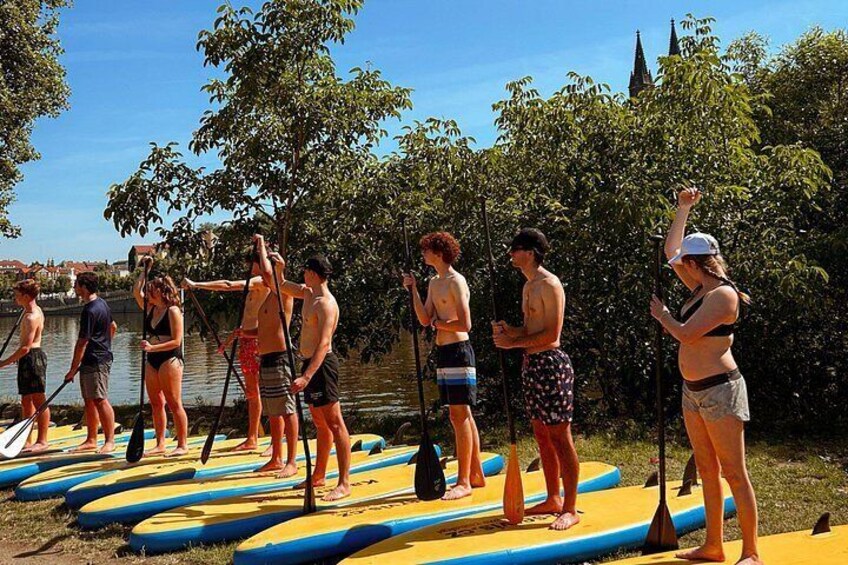 People standing on paddleboards by a lake, some holding paddles. 3
