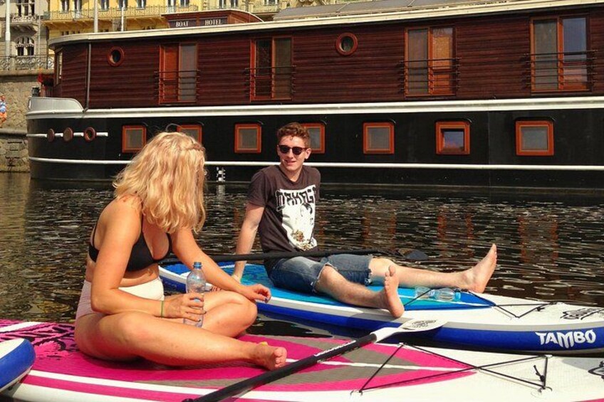 Zwei Personen auf einem Stand-Up-Paddleboard in der Nähe eines Holzboots. 2