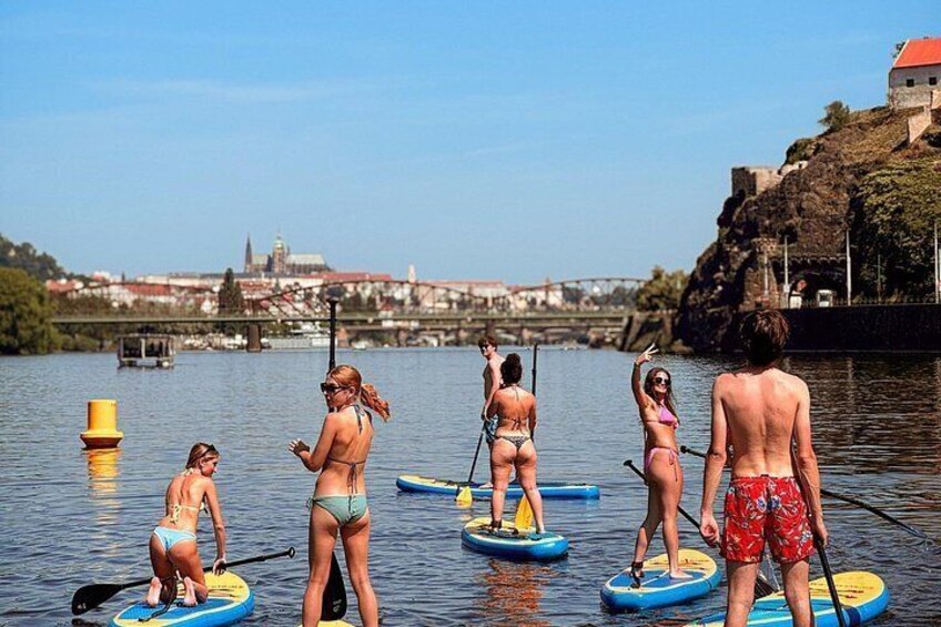 People paddleboarding on a calm river with a historic bridge and castle in the background. 4