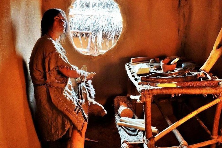 Una persona in abiti tradizionali, un cesto di vimini e una struttura con tetto di paglia. 1