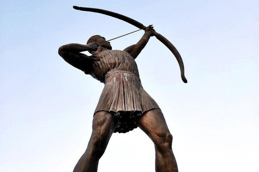 Una estatua de bronce de una figura con arco y flecha, vestida con una túnica, sobre un cielo despejado. 2