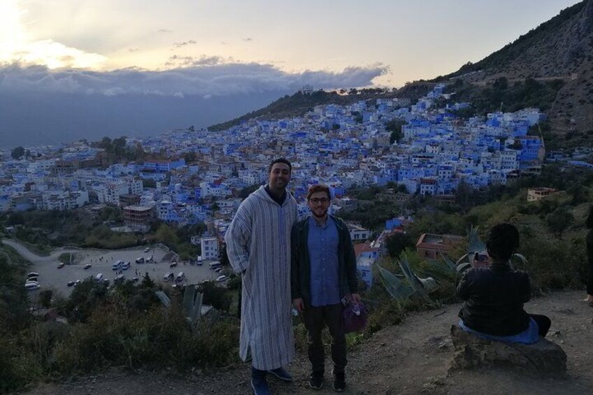 Two people standing on a path with a view of a town with blue buildings. 2