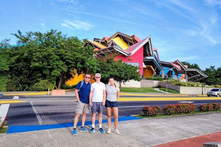 Un bâtiment aux couleurs vives, doté d’une architecture originale, une zone pavée avec une ligne bleue, et une voiture garée à l’arrière-plan. 2