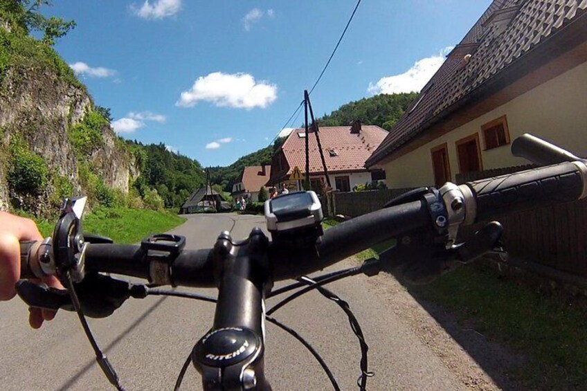 A bicycle's handlebars with a GPS device, a road, houses, and a cliff. 3