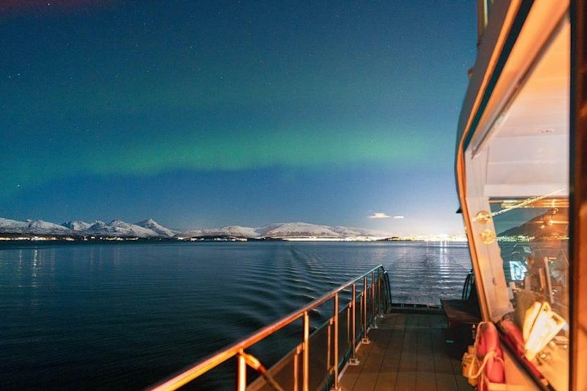 A boat on a calm body of water with snow-capped mountains in the distance and the Northern Lights in the sky. 3