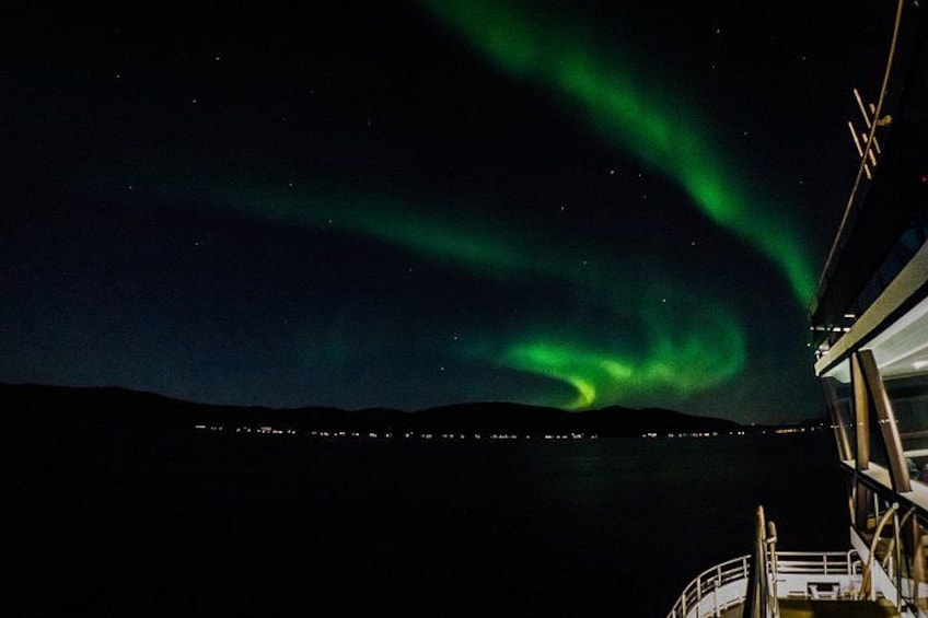 The Northern Lights over a dark landscape with a boat and distant lights. 5