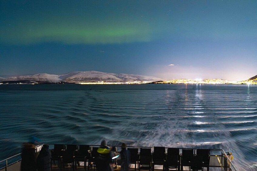 A boat on calm water with a view of snow-capped mountains and the northern lights in the sky. 4