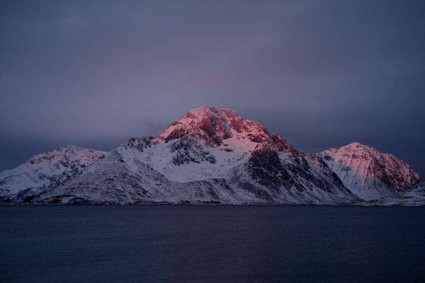 A snow-covered mountain range with a body of water in the foreground. 2