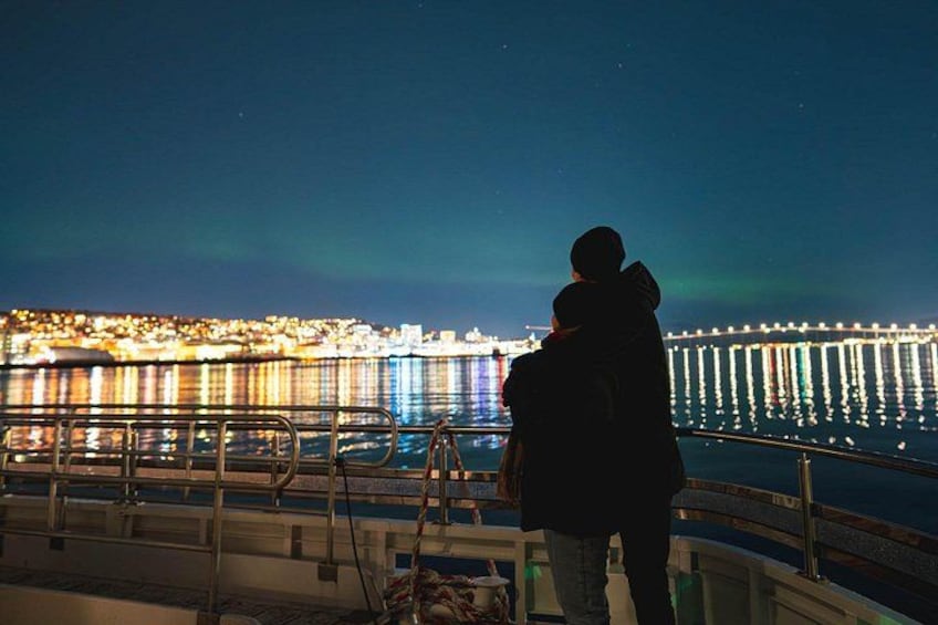 A person standing on a balcony overlooking a waterfront with a brightly lit pier and a cityscape in the background. 5