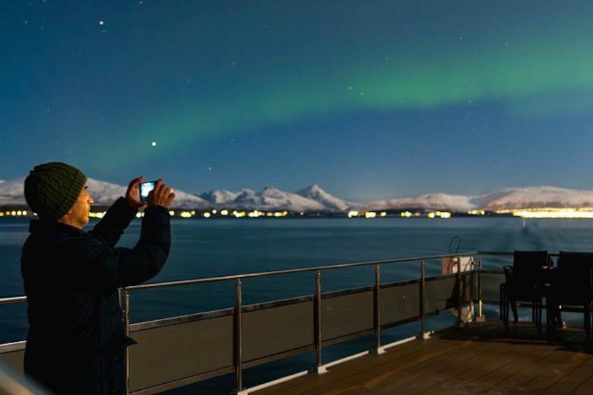 A person taking a photo of the aurora borealis with snow-capped mountains in the background. 3