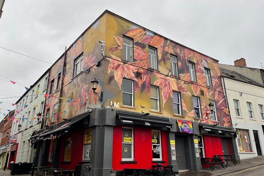 Un edificio con un mural colorido de hojas, un toldo rojo y un letrero que dice 'TENNIS'. 1