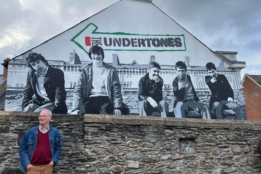 A mural of five men on a wall with the word "UNDERTONES" and a green arrow pointing left. 1