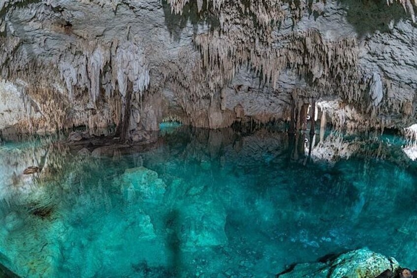 A cave with stalactites and stalagmites, clear turquoise water, and a rocky bottom. 5