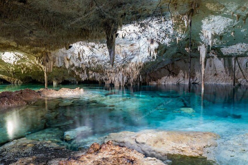 Una cueva con agua turquesa cristalina, estalactitas y un primer plano rocoso. 3