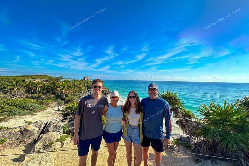 Un grupo de personas de pie en una playa, con cielo azul y un océano en el fondo. 1