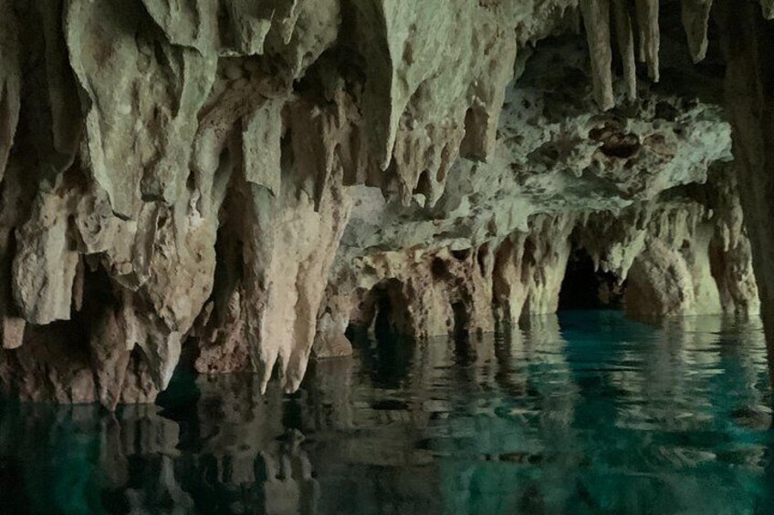 A cave interior with stalactites and stalagmites, and a pool of water at the bottom. 5