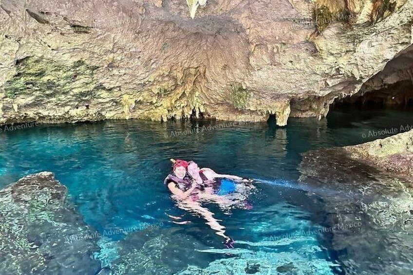 A person swimming in a clear blue pool with rocky cave walls. 2