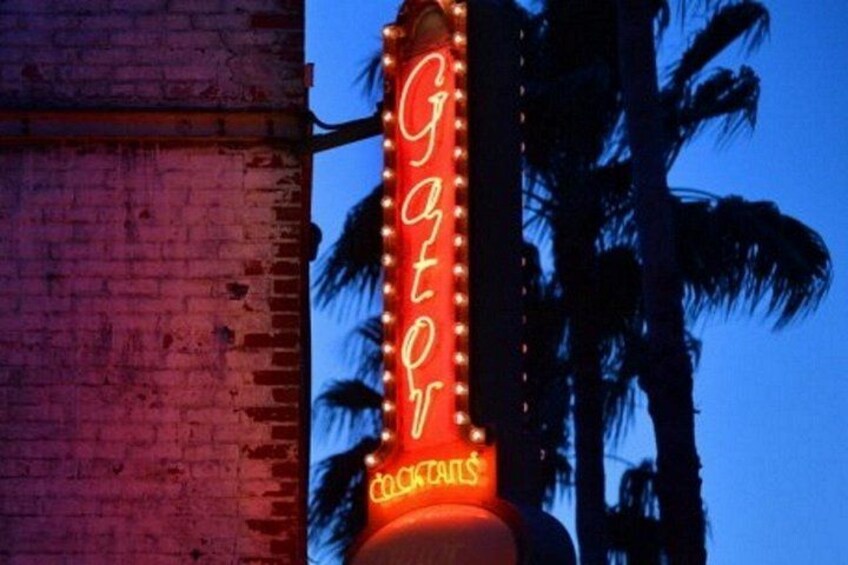 A neon sign with the word 'Gator' and 'COCKTAILS' against a dusk sky, with palm trees in the background. 3