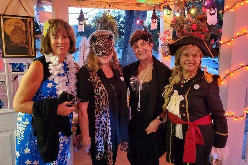 Four people in costumes, a decorated interior with string lights, and Halloween-themed decorations. 4