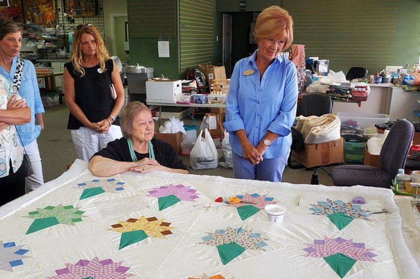 En grupp människor i ett rum, med ett stort lapptäcke på ett bord. 3